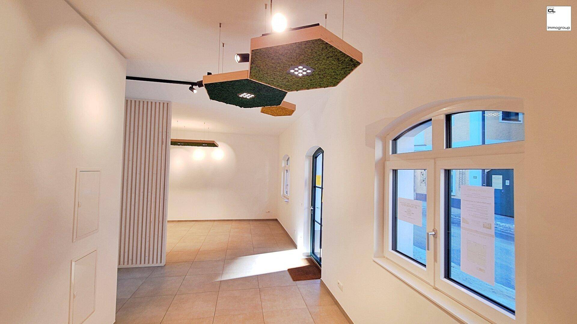 Lichtdurchfluteter Raum mit Fliesenboden, hohen Decken und modernen Deckenleuchten.