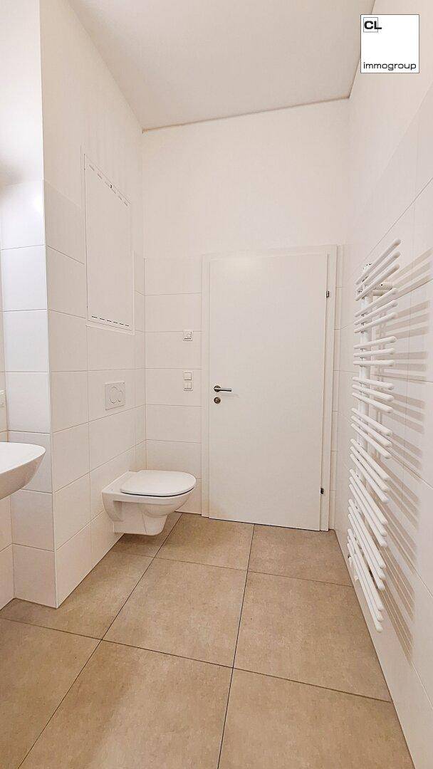 Helles Badezimmer mit weißen Fliesen, wandhängendem WC und beheiztem Handtuchhalter.