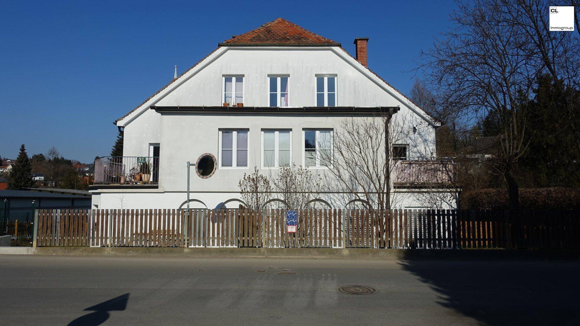 Gepflegtes Wohnhaus mit weißer Fassade, Satteldach und kleinen Balkonen in sonniger Umgebung.