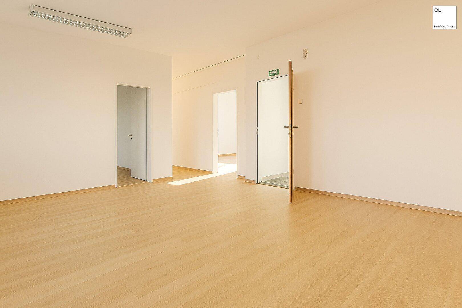 Langer, heller Flur oder Großraumbüro mit Holzboden und mehreren Türen zu angrenzenden Räumen.