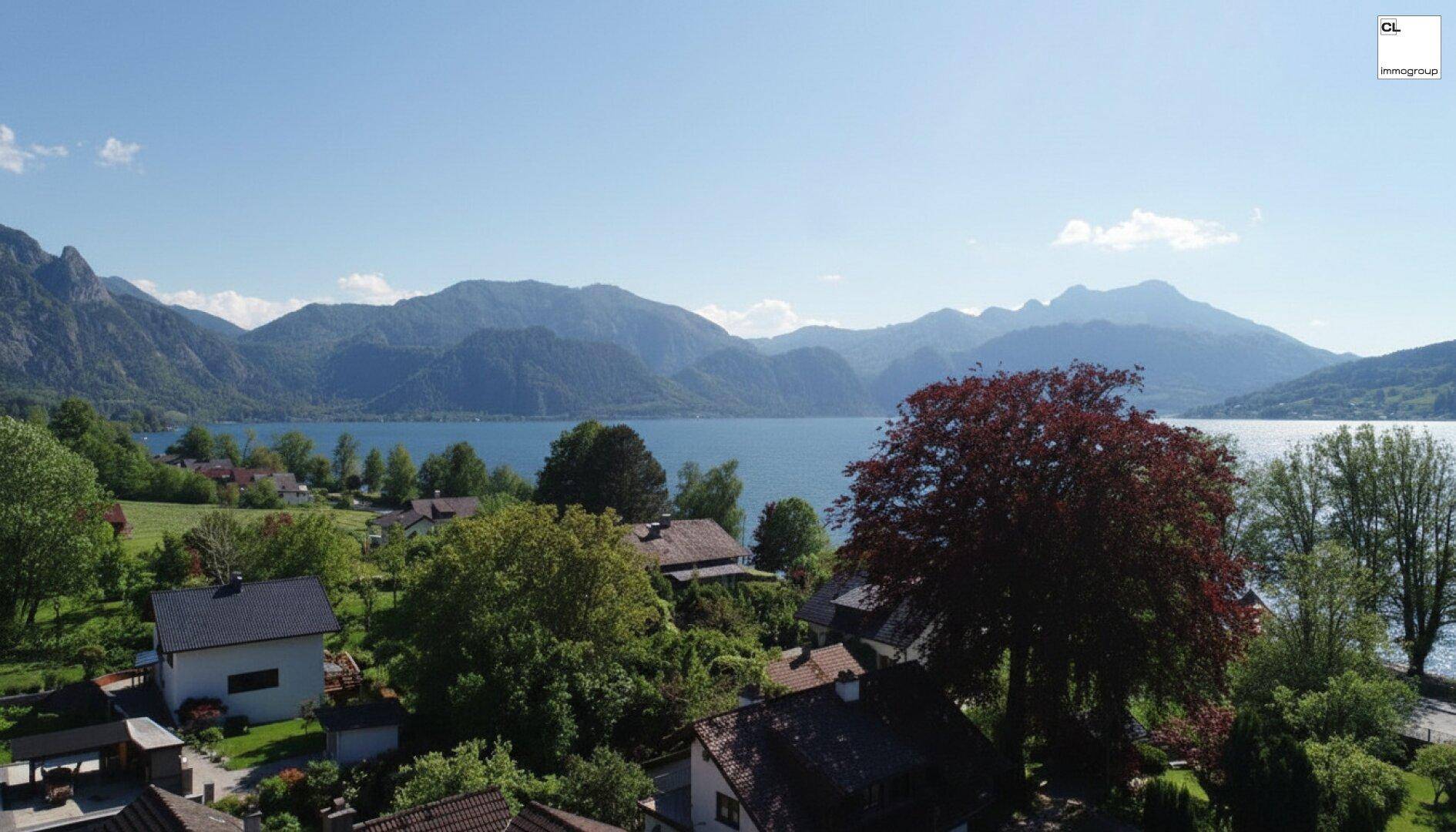 Weitläufige Luftaufnahme einer Wohngegend am See mit beeindruckendem Bergpanorama unter blauem Himmel.
