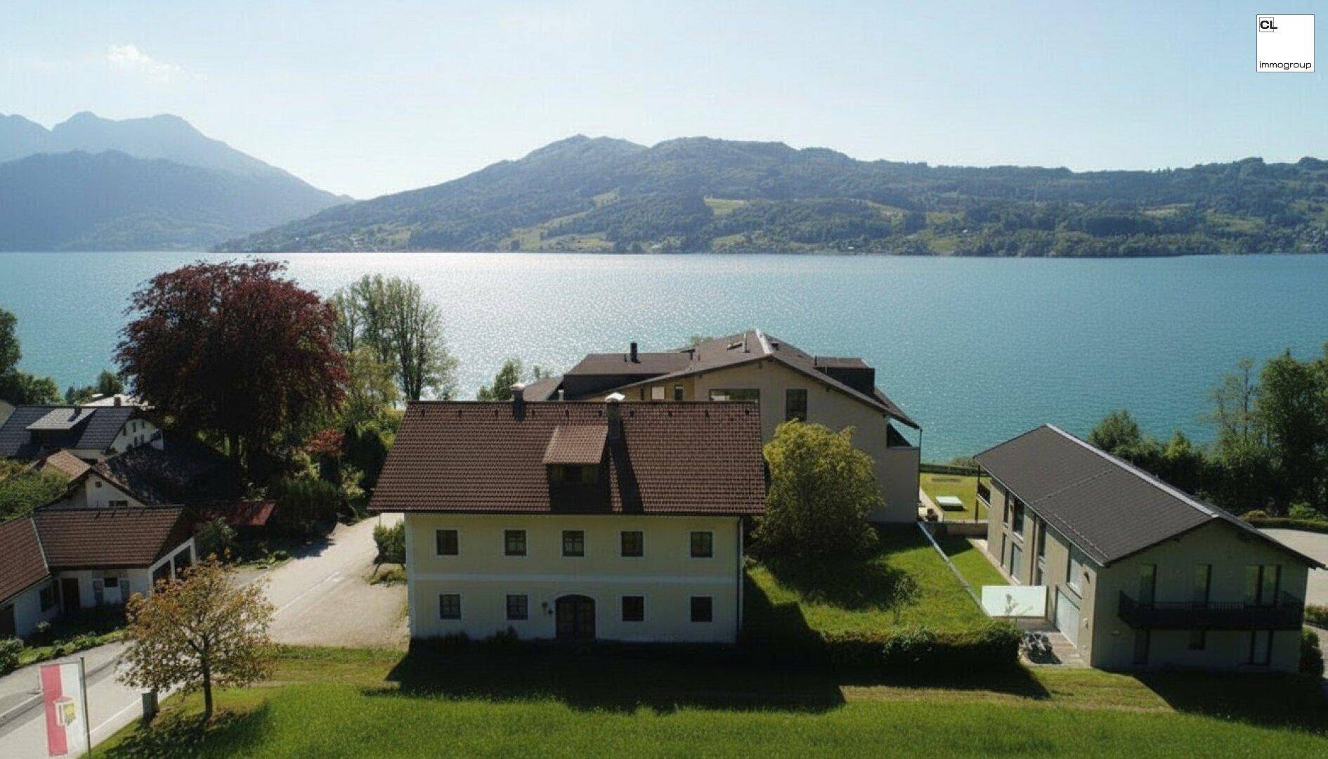 Panoramablick auf ein Seegrundstück mit mehreren Gebäuden und einer malerischen Bergkulisse.