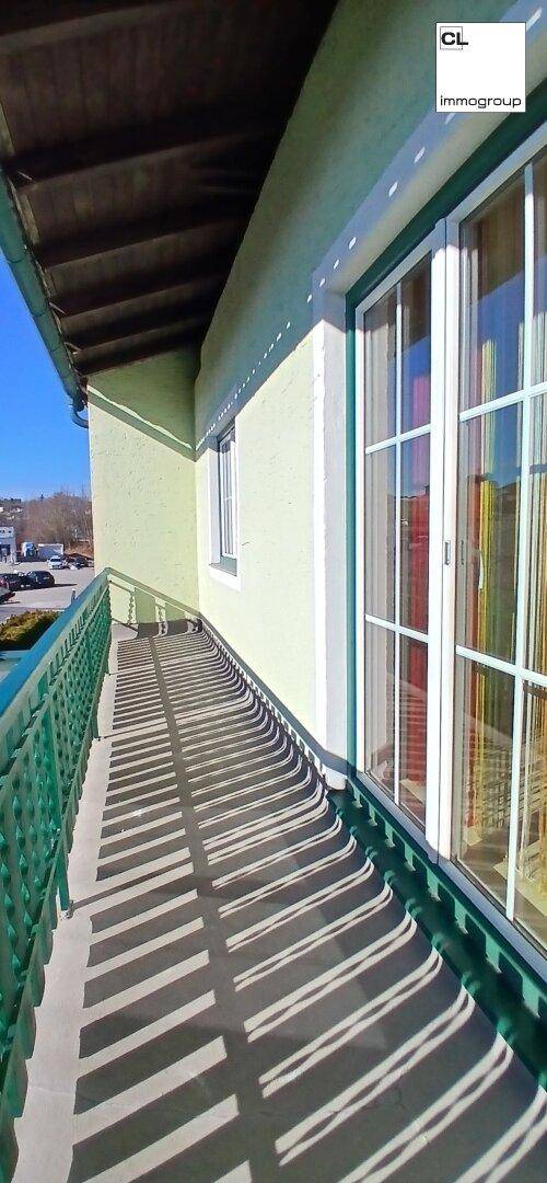 Langer Balkon mit grüner Brüstung und großen Fenstern, die Schatten auf den Boden werfen.