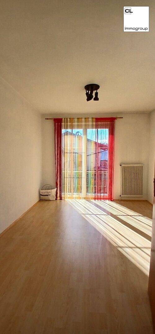 Heller, leerer Raum mit hellem Holzboden, großem Fenster und farbigen Vorhängen, ideal für Wohnzwecke.