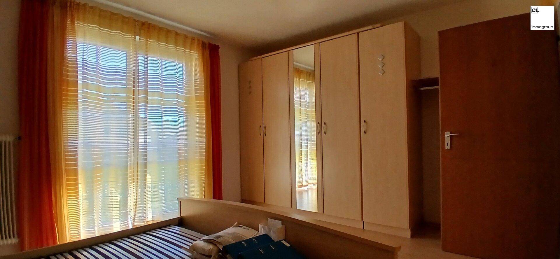 Gemütliches Schlafzimmer mit großem Kleiderschrank, Spiegel und farbenfrohen Vorhängen am Fenster.