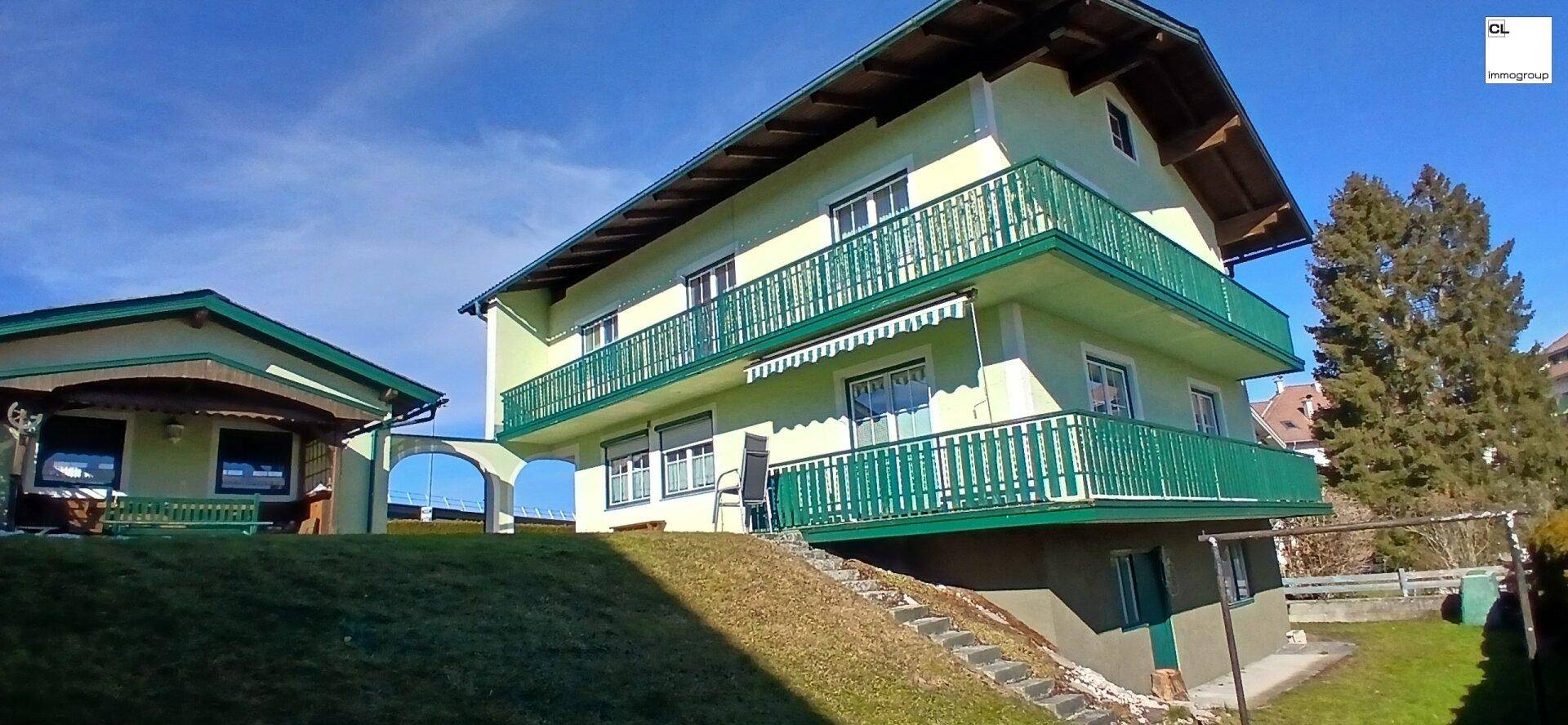 Wohnhaus mit mehreren Balkonen und Garten auf einem Hanggrundstück bei sonnigem Wetter.