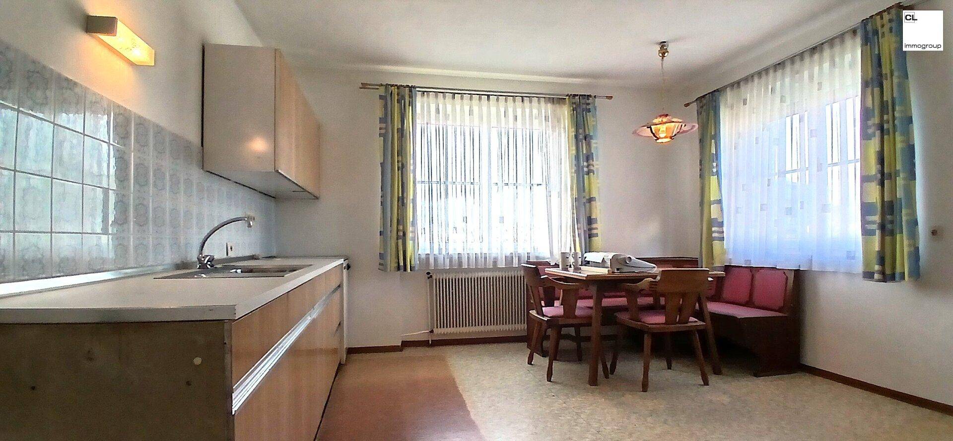 Einfache Küche mit Essbereich, Fliesenrückwand und Fenster mit Vorhängen.