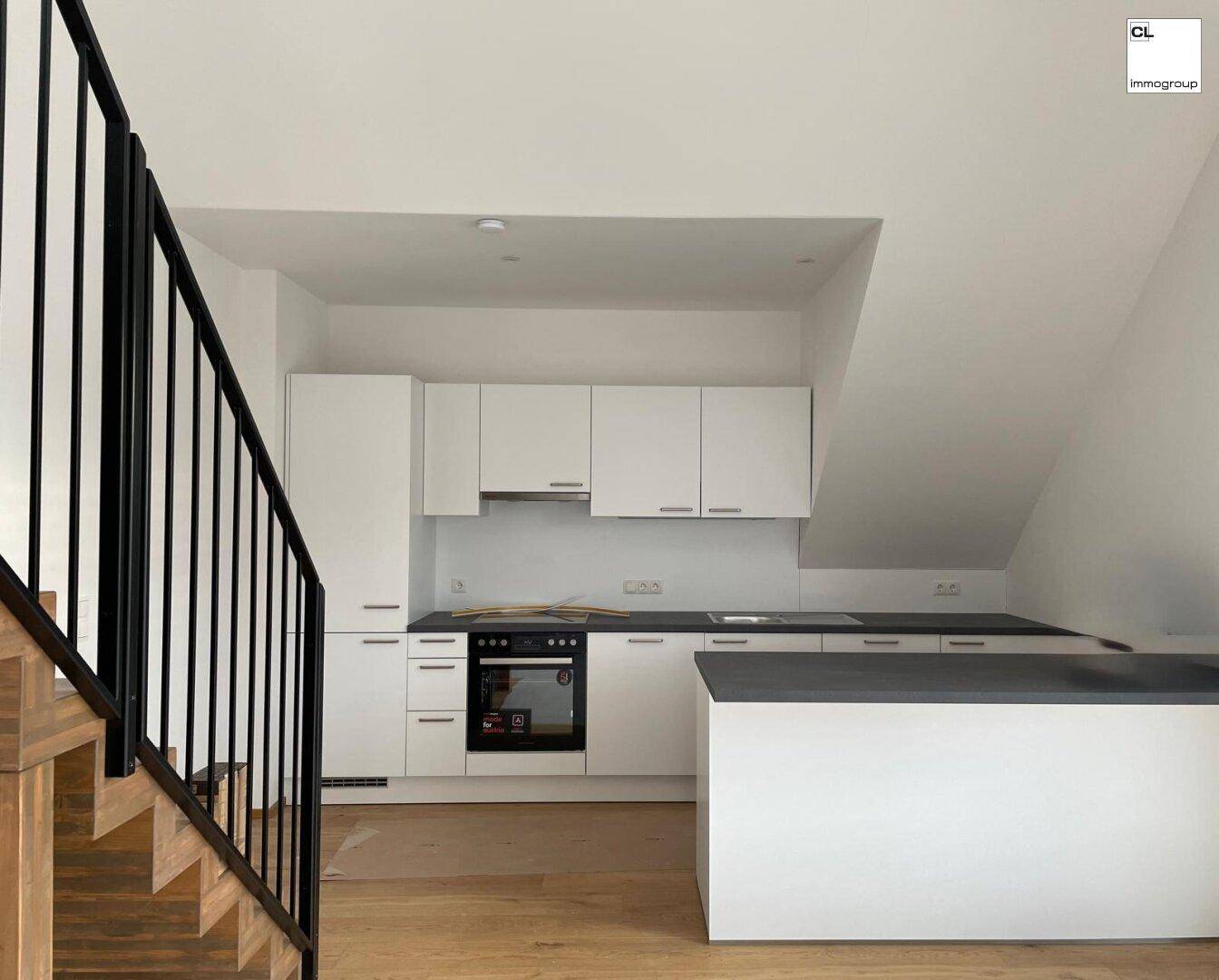 Moderne Einbauküche mit weißen Schränken, dunkler Arbeitsplatte und Dachschräge.