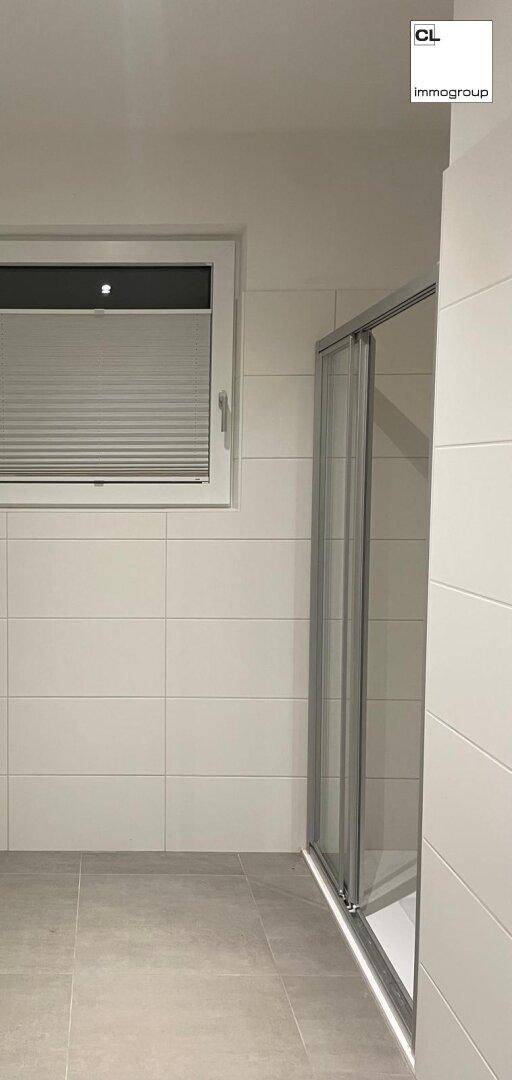 Modernes Badezimmer mit Duschkabine, hellen Fliesen und Fenster für Tageslicht.