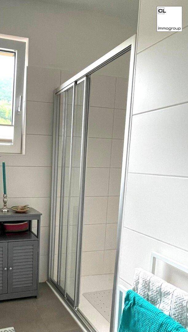 Helles Badezimmer mit Duschkabine, Fenster und Handtuchhalter.