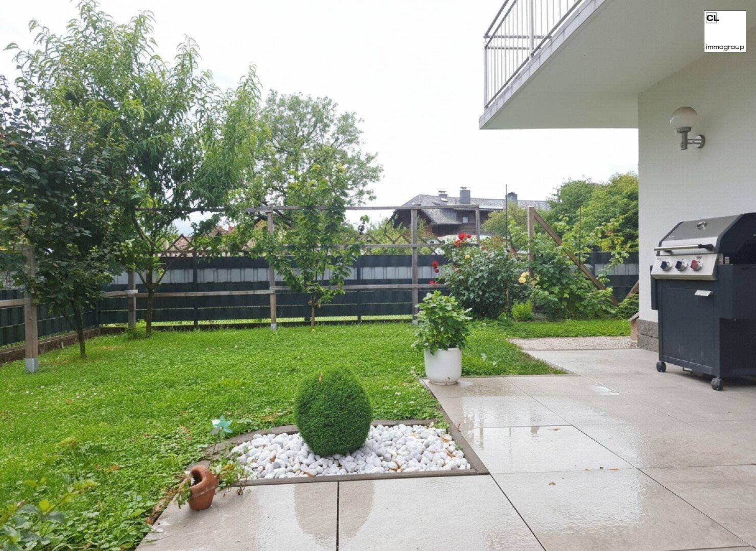 Gepflasterte Terrasse mit Rasenfläche, Bäumen und einem Grill, ideal für Mahlzeiten im Freien.