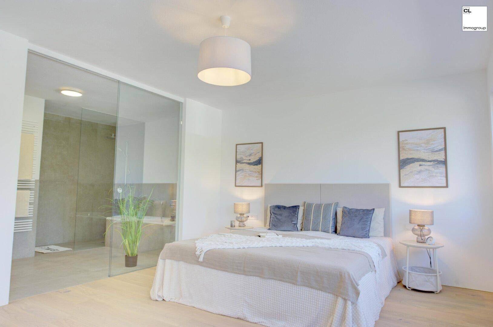 Modernes Schlafzimmer mit Doppelbett und offenem Zugang zu einem eleganten Badezimmer durch eine Glaswand.