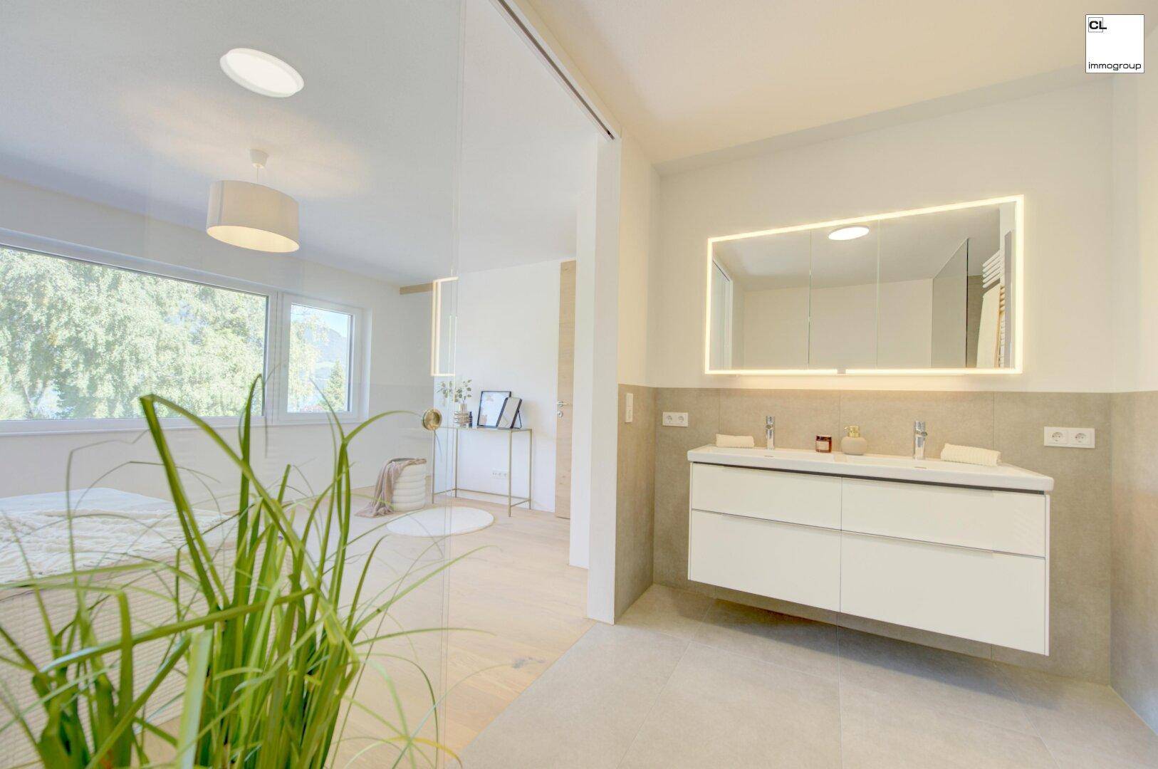 Modernes Badezimmer mit Doppelwaschbecken, beleuchtetem Spiegel und Fenster, offen zum Schlafzimmer.