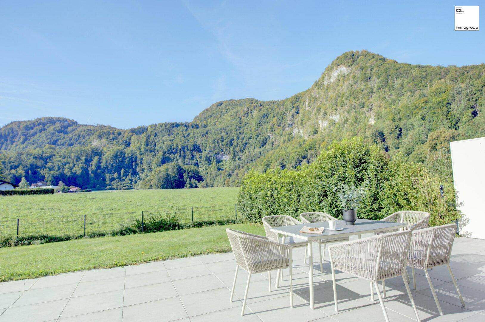 Sonniger Terrassenbereich mit Esstisch und Stühlen, umgeben von grünen Wiesen und majestätischen Bergen.