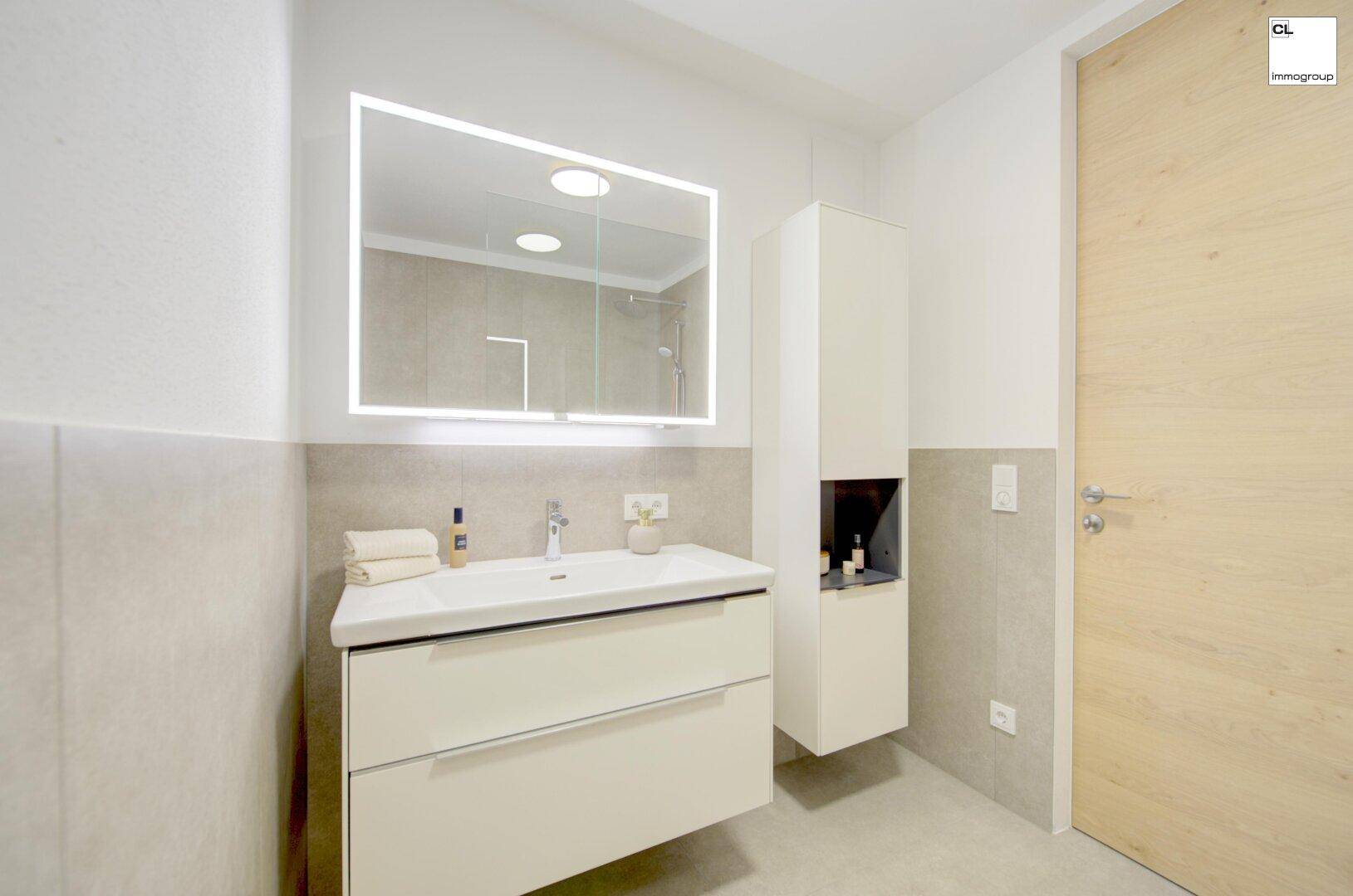 Modernes Badezimmer mit Waschtisch, beleuchtetem Spiegel und hellen Fliesen.