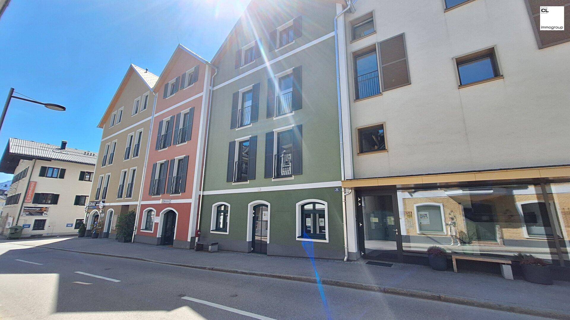 Mehrere Gebäude mit farbigen Fassaden und traditionellen Fensterläden an einer sonnigen Straße.