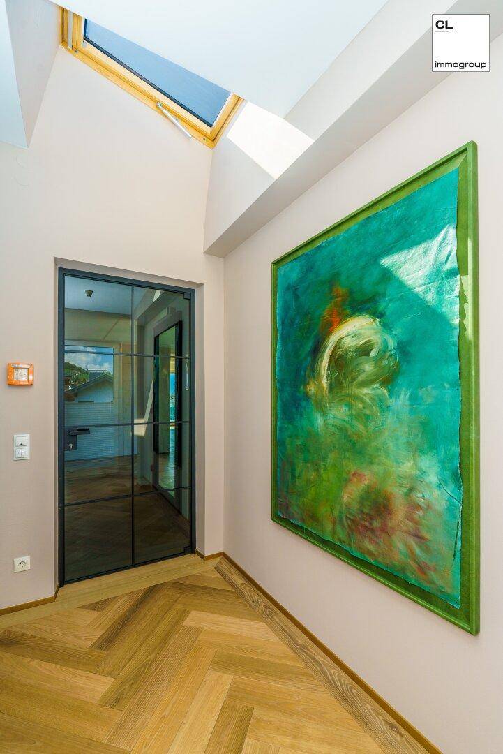 Heller Flur mit Fischgrätparkett, Oberlicht und moderner Kunst an der Wand.