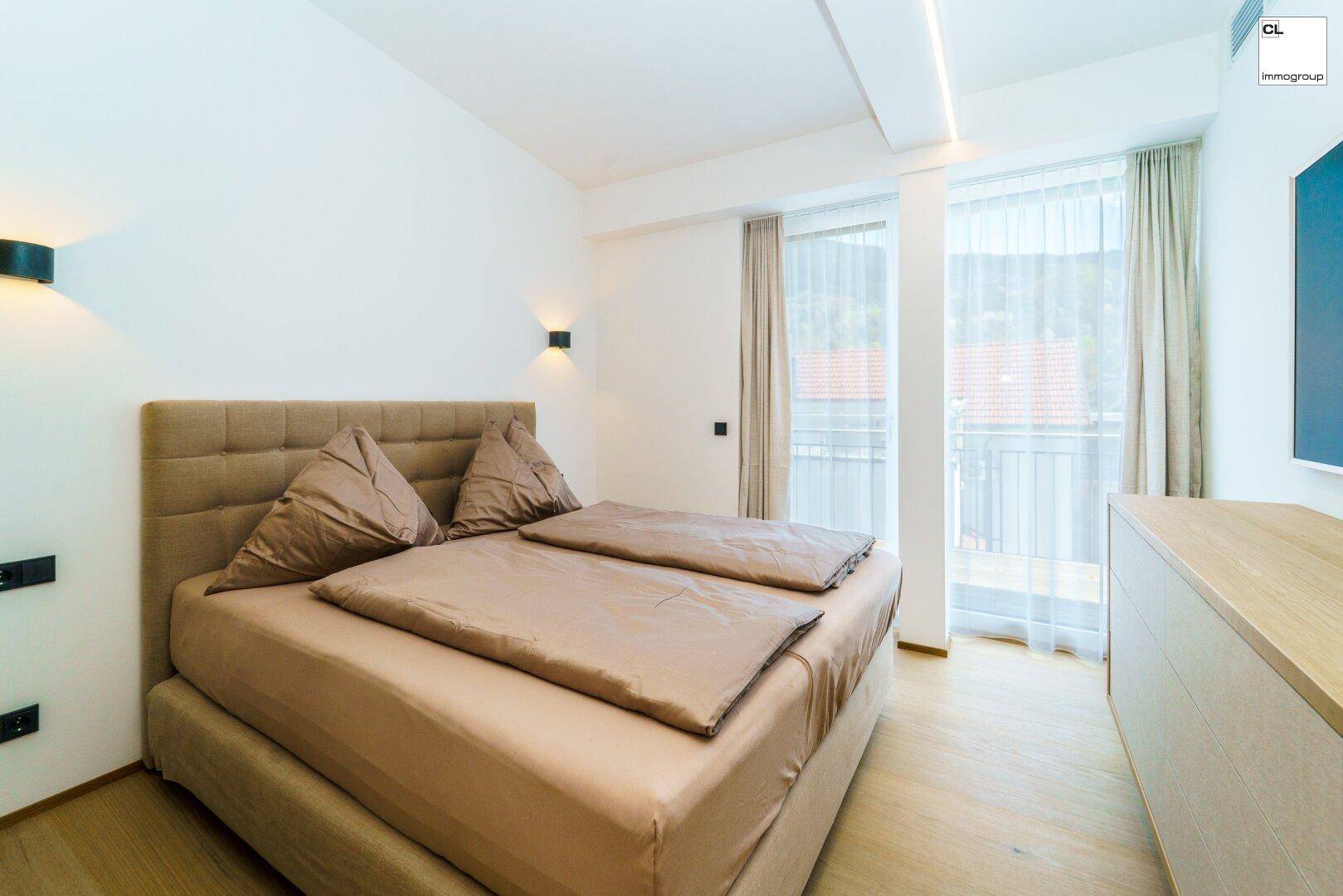 Helles Schlafzimmer mit Doppelbett, Holzboden und Zugang zu einem kleinen Balkon.