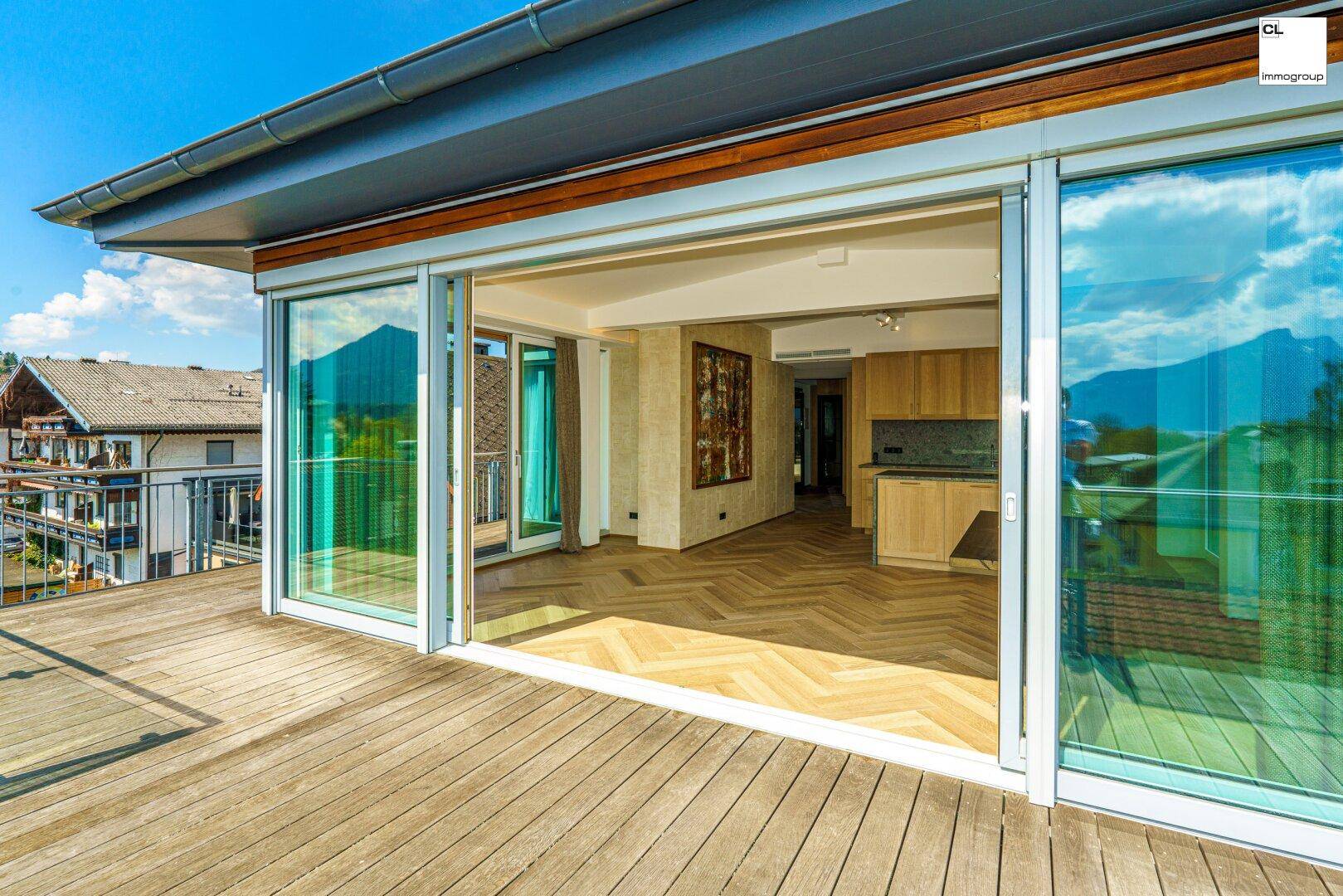 Offener Wohnbereich mit Holzboden und Zugang zu einer großen Terrasse mit Bergblick.