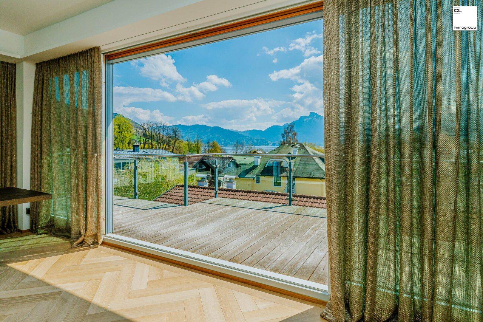 Lichtdurchfluteter Raum mit raumhohen Fenstern und atemberaubendem Blick auf See und Berge.