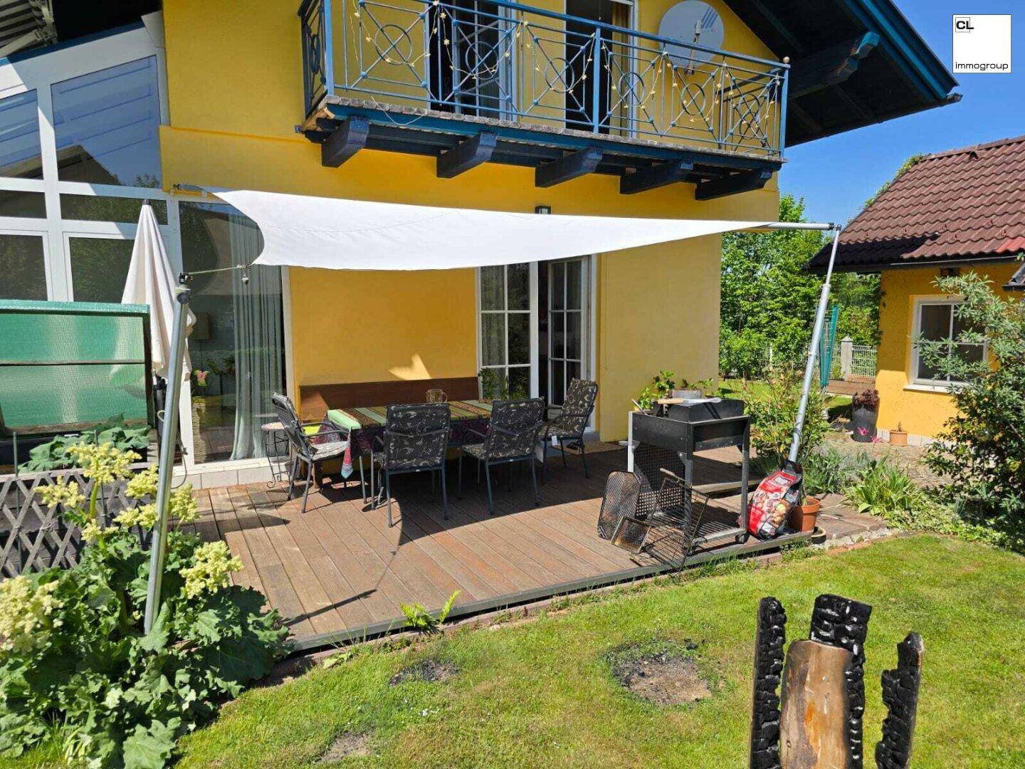 Gemütliche Holzterrasse mit Esstisch, Sonnensegel und Grillbereich, ideal für Mahlzeiten im Freien.