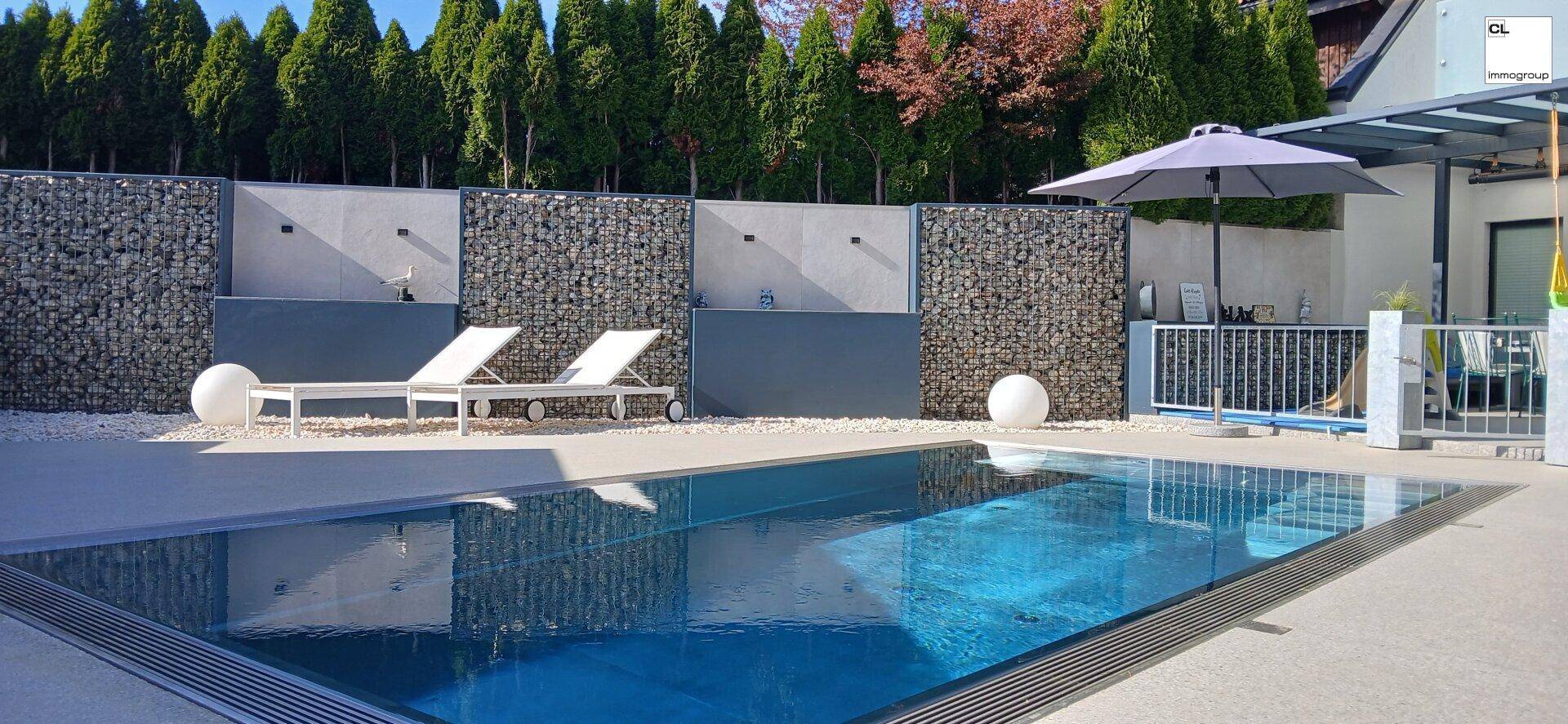 Großzügiger Poolbereich mit Sonnenliegen und Gabionenwänden für Privatsphäre.