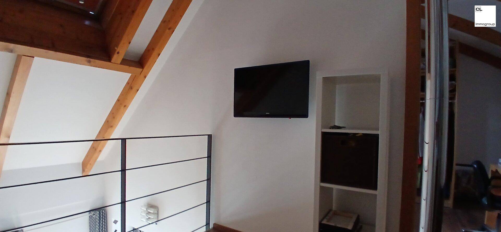 Dachgeschossbereich mit sichtbaren Holzbalken, Dachschräge und Fernseher.