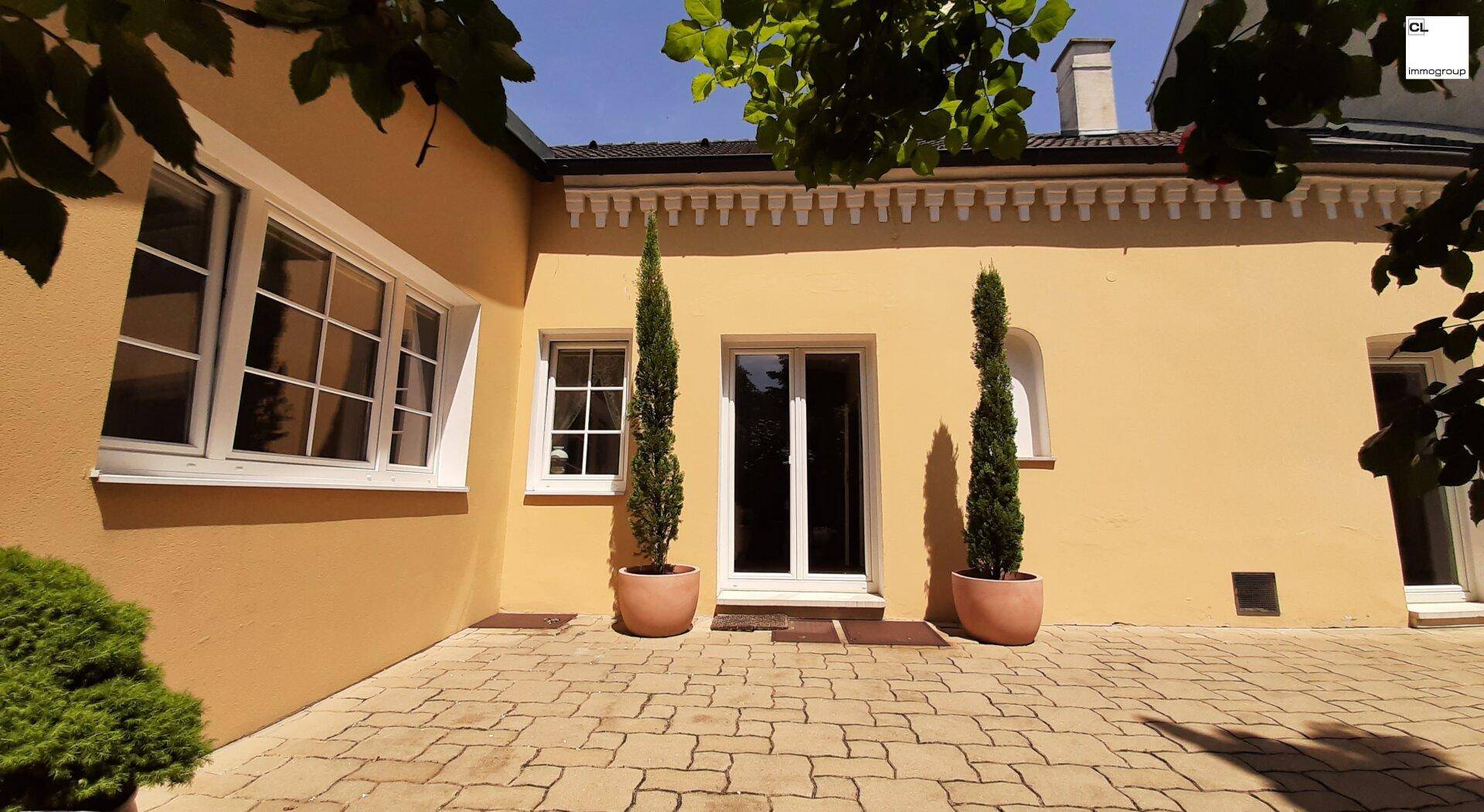 Sonniger Terrassenbereich mit gepflastertem Boden und Zugang zum Haus durch eine Glastür.