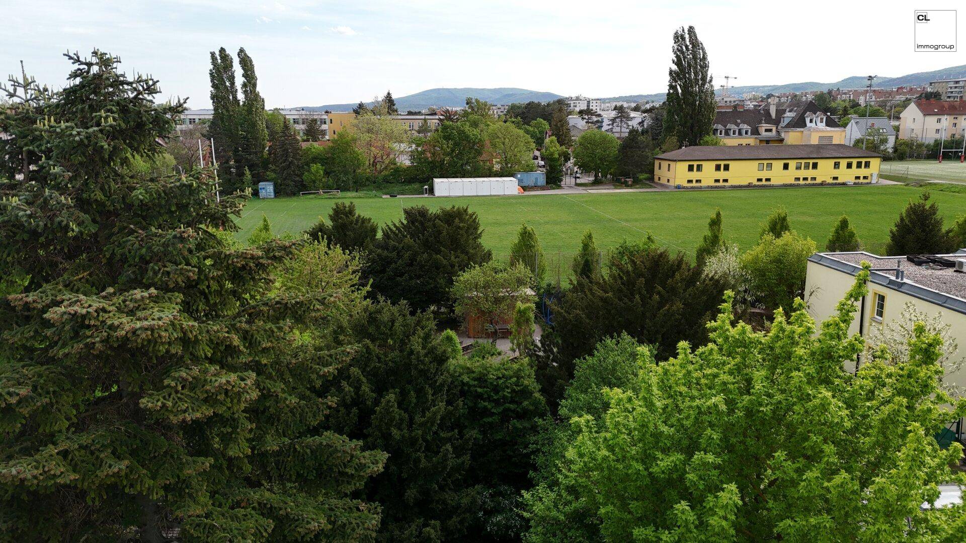 Weitläufiger Blick über eine grüne Sportanlage und umliegende Gebäude in der Nachbarschaft.