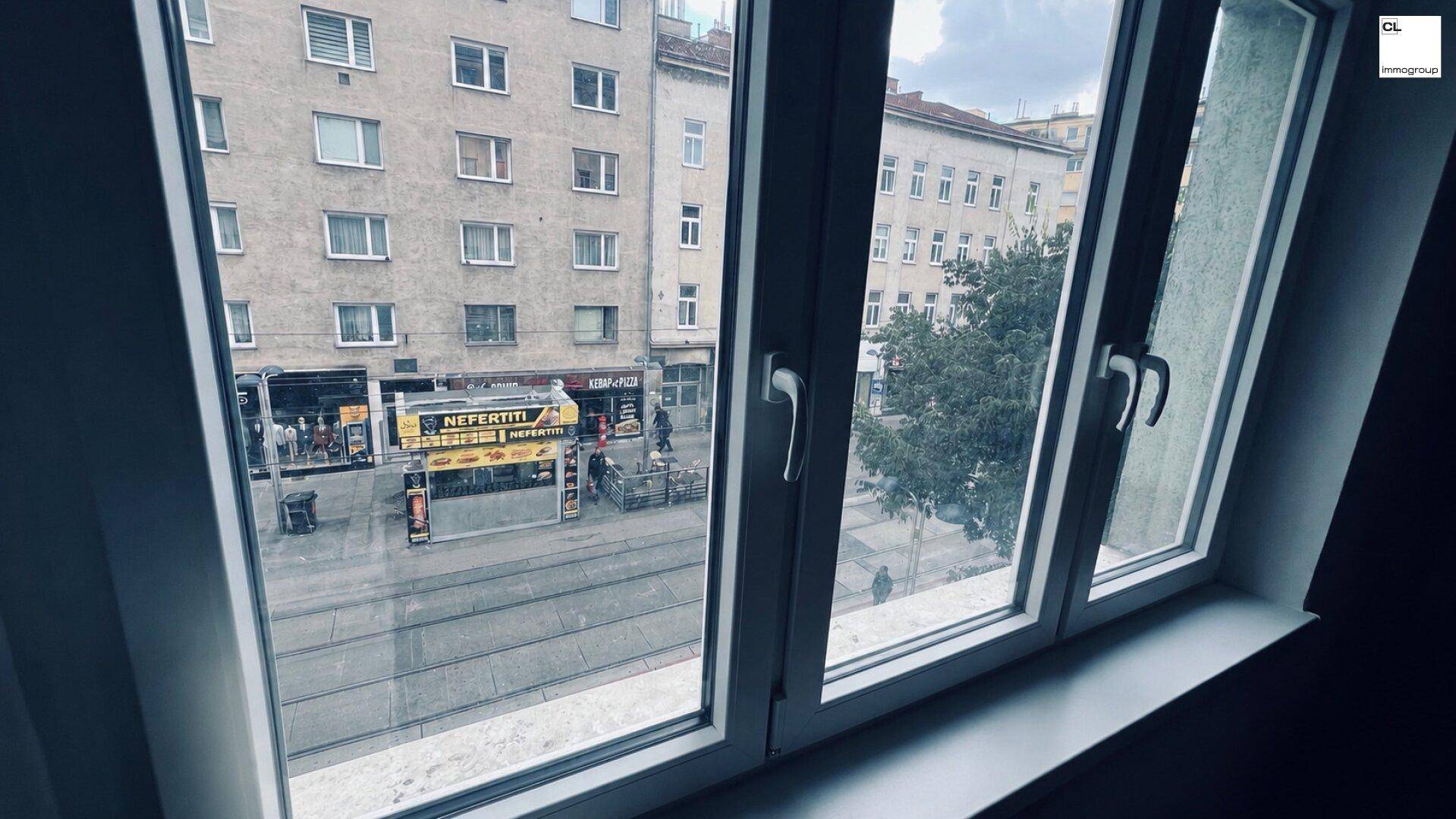 Blick aus dem Fenster auf eine belebte Straße mit Straßenbahn und umliegenden Stadtgebäuden.