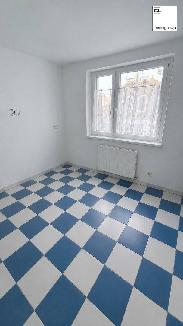 Leeres Zimmer mit weiß gestrichenen Wänden und einem auffälligen blau-weiß karierten Fliesenboden.