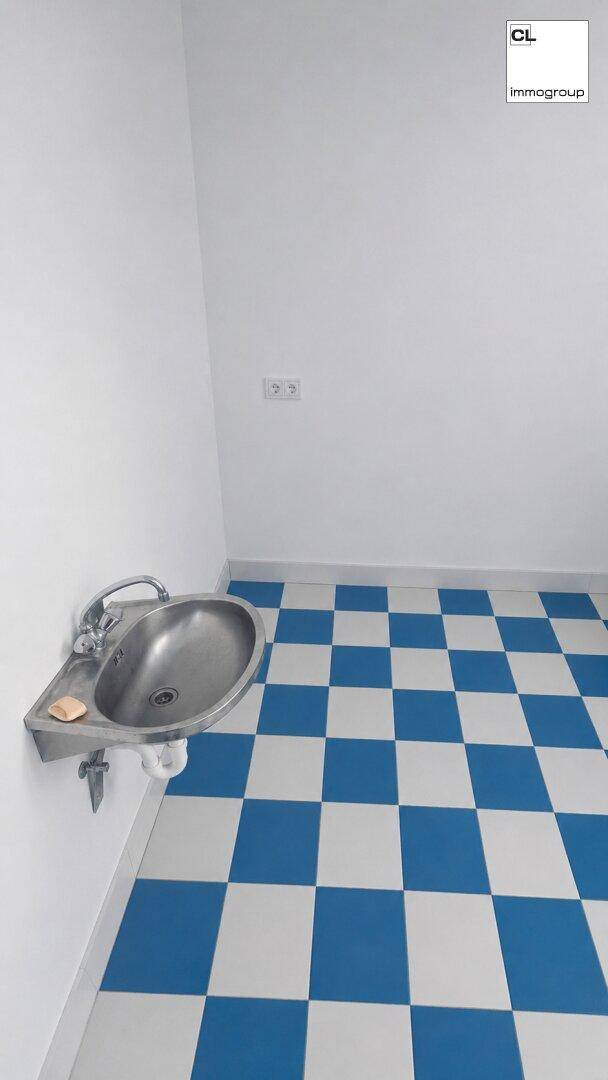 Kleiner Raum mit einem Edelstahlwaschbecken und einem blau-weiß karierten Fliesenboden.