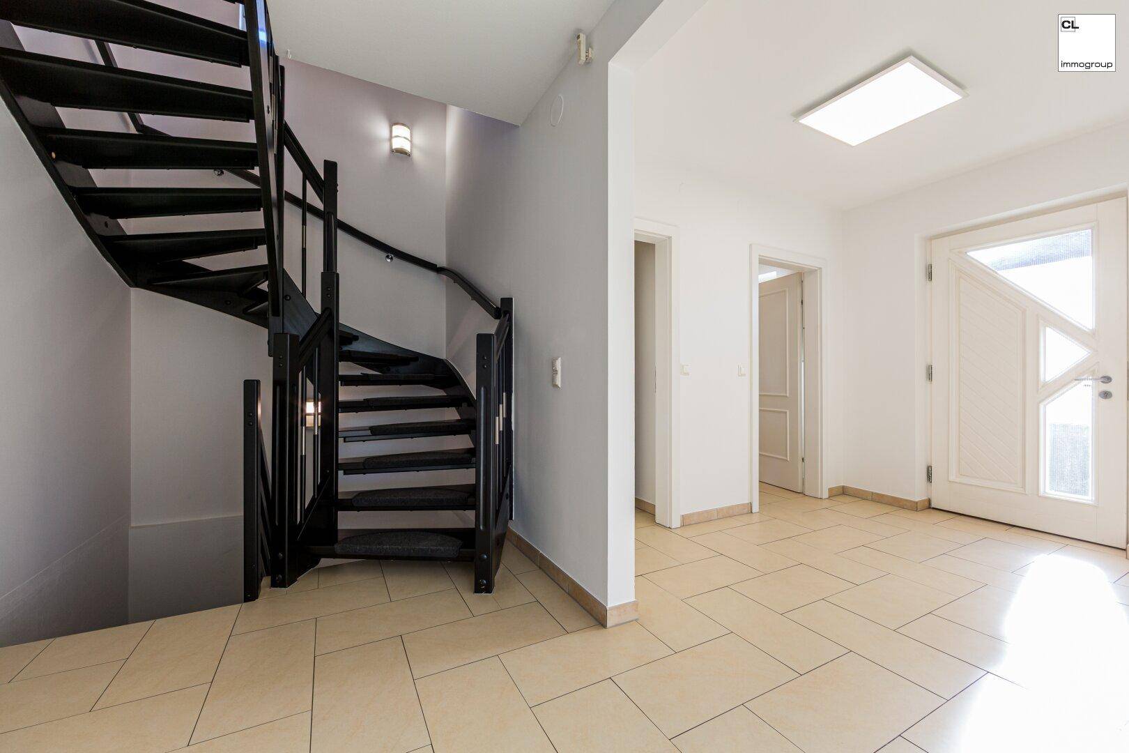 Geräumiger Flur mit schwarzer Wendeltreppe, hellem Fliesenboden und weißer Eingangstür.