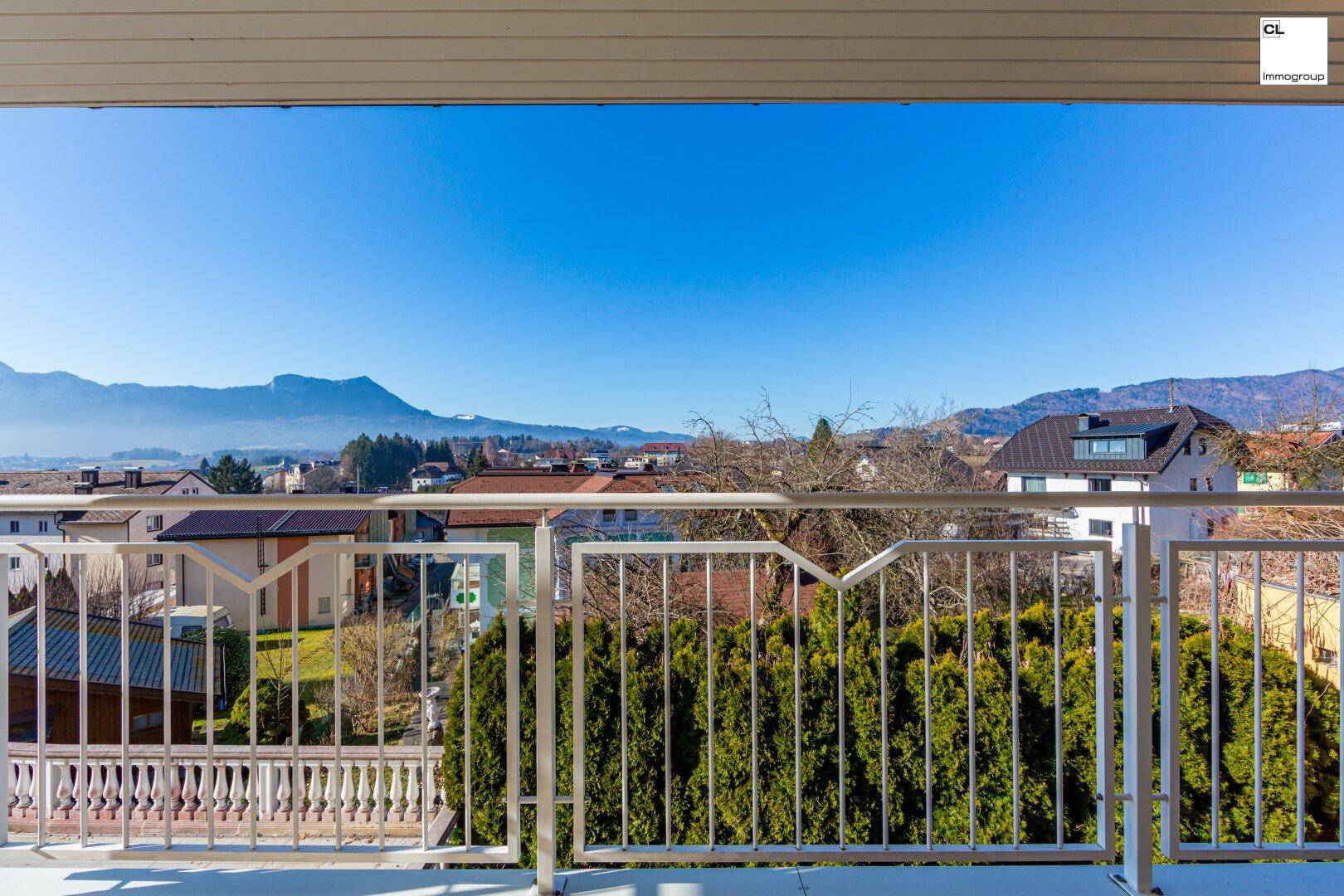 Balkon mit Metallgeländer und Blick auf die umliegende Wohngegend und grüne Hecken.