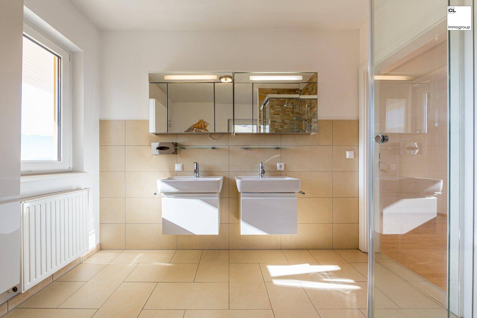 Modernes Badezimmer mit Doppelwaschbecken, Spiegelschrank, Dusche und Fenster.