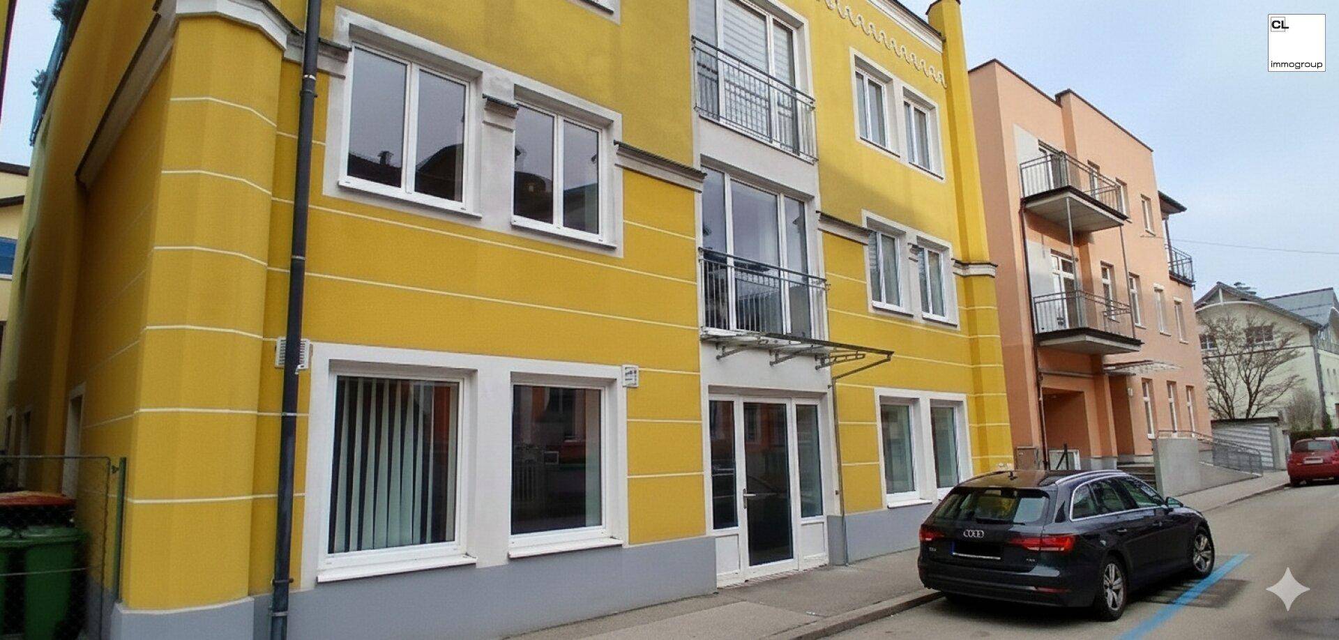 Gelbe Fassade eines Mehrfamilienhauses mit weißen Fenstern und Balkonen an einer Straße.