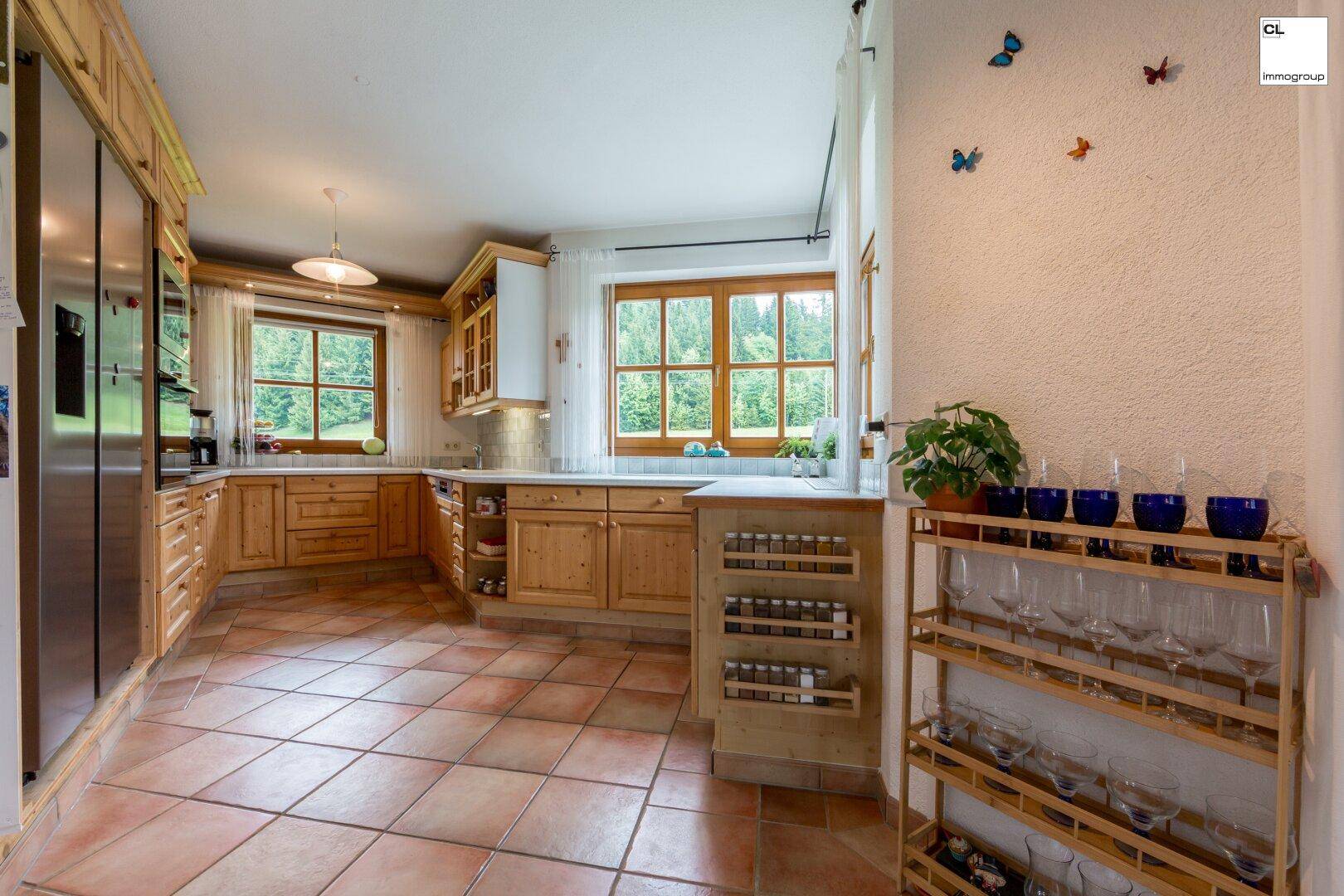 Geräumige Holzküche mit Terrakottafliesen, viel Stauraum und Fenstern mit Waldblick.