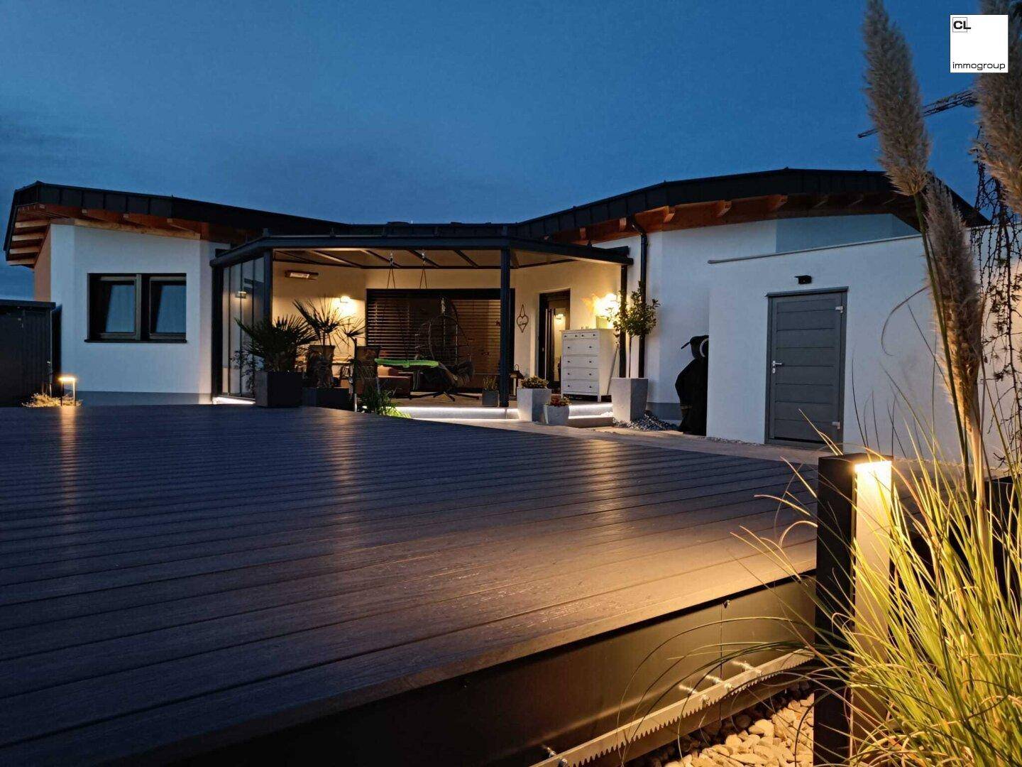 Große Holzterrasse mit stimmungsvoller Beleuchtung am Abend und überdachtem Sitzbereich.