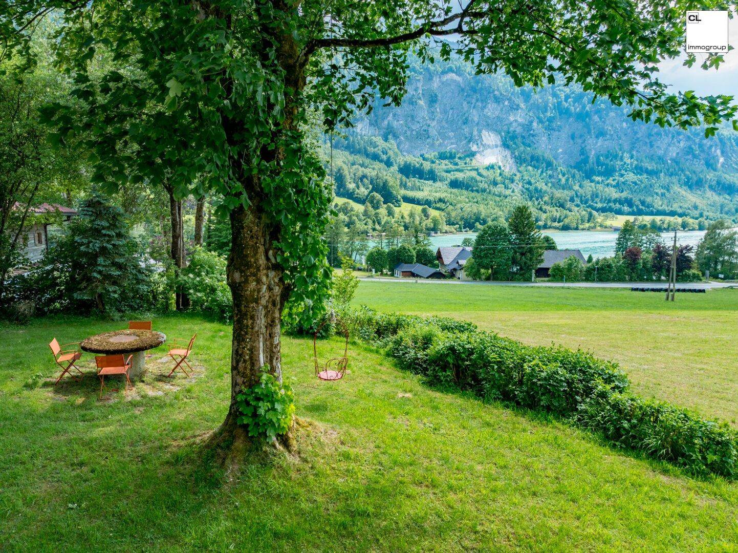 Malerischer Gartenbereich mit Schaukel unter einem Baum und weitem Blick auf den See und die Berge.