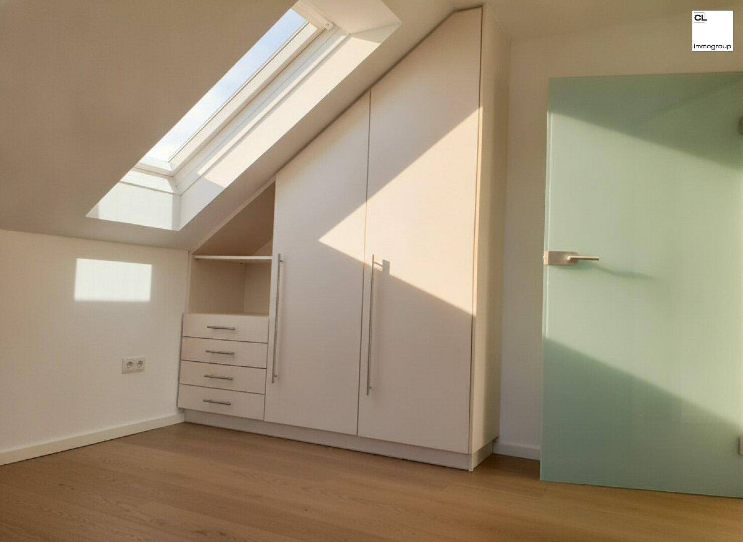 Helles Zimmer mit Einbauschrank, Holzboden, Dachschräge und einem Dachfenster für natürliche Belichtung.