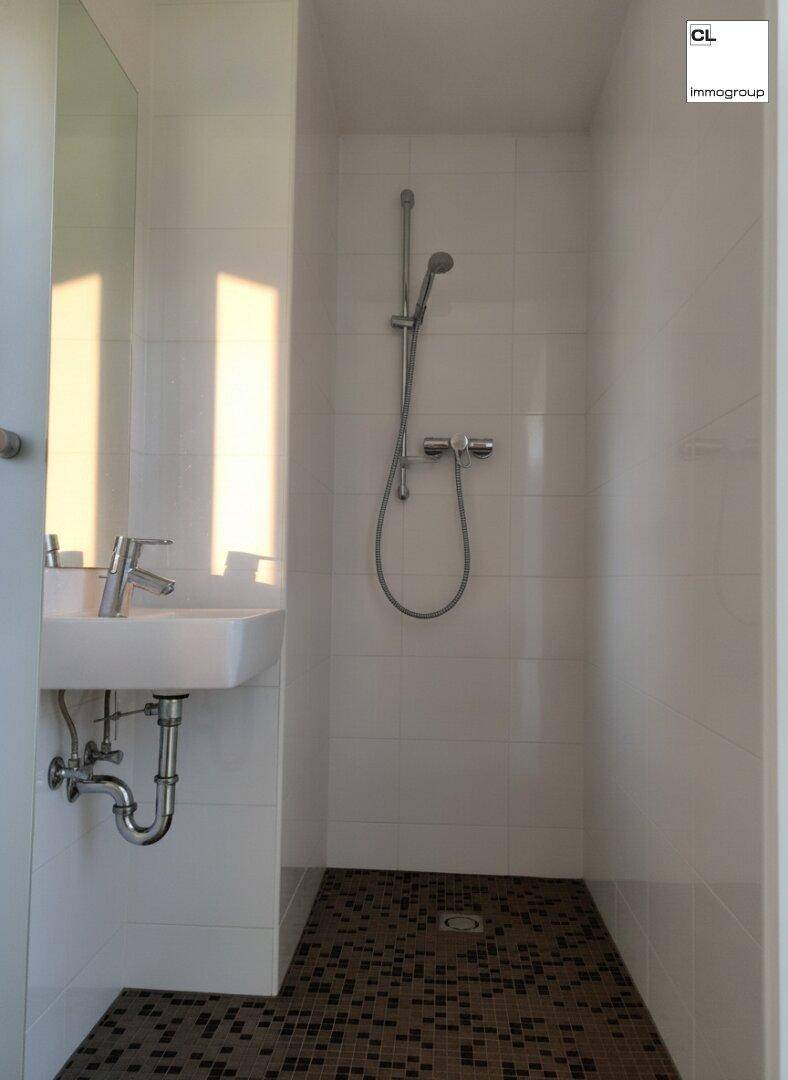 Kompaktes Badezimmer mit Duschbereich, Einzelwaschbecken und weißen Fliesen an Wänden und Boden.