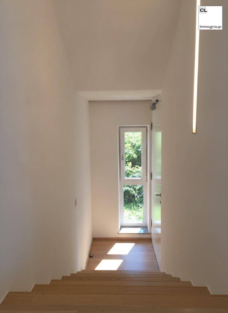 Heller Treppenaufgang mit Holzstufen, weißen Wänden und einem Fenster, das natürliches Licht hereinlässt.