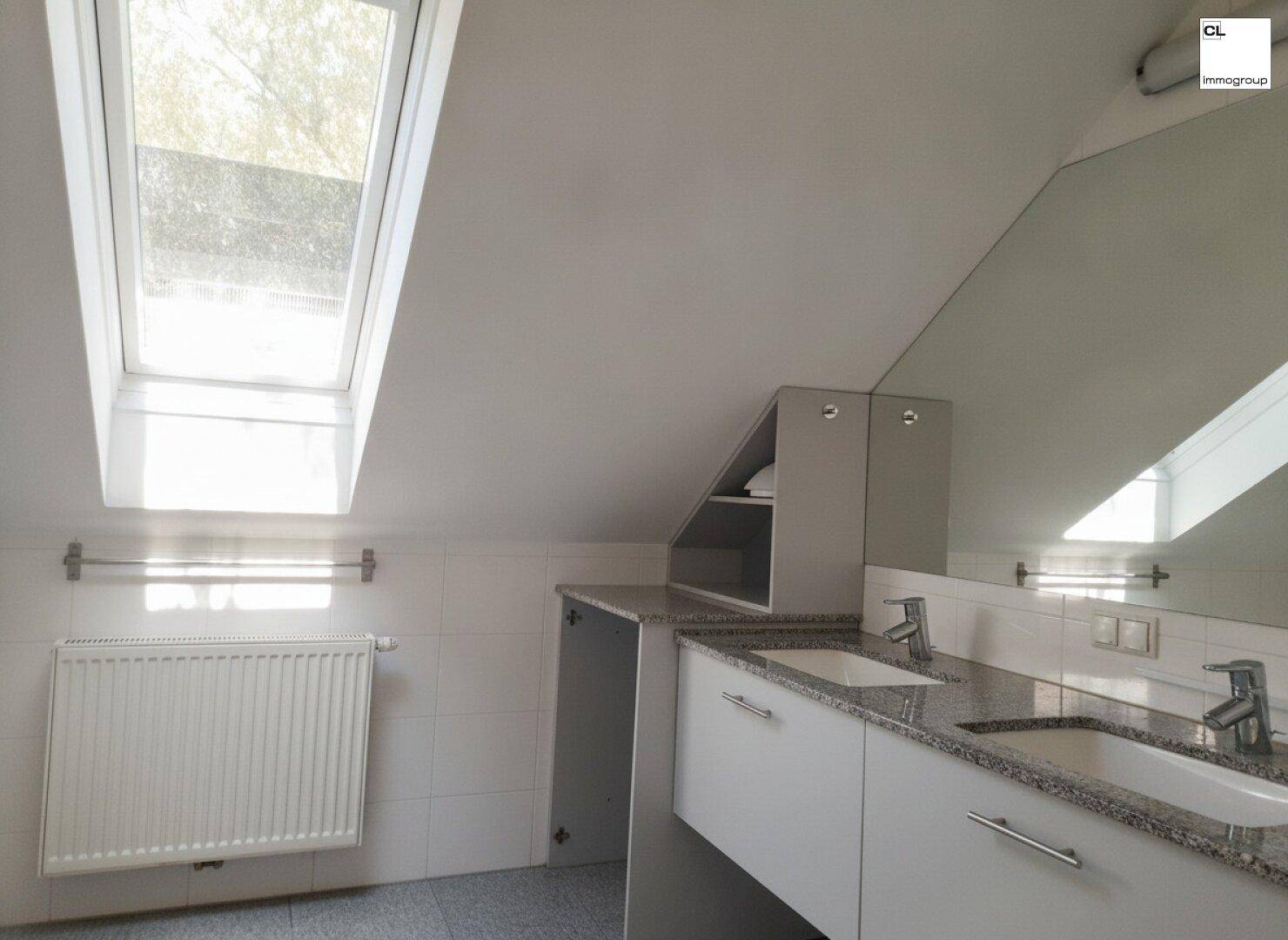 Helles Badezimmer mit Doppelwaschbecken, Heizkörper, gefliesten Wänden und einem großen Dachfenster.