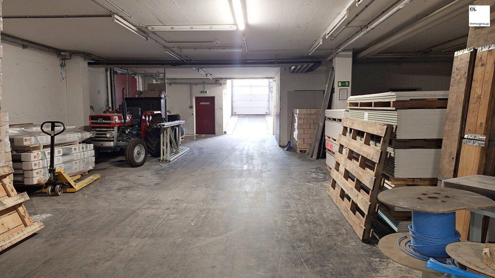Lagerhalle mit Betonboden, hohen Decken, Paletten und einem Traktor, bereit für den Betrieb.