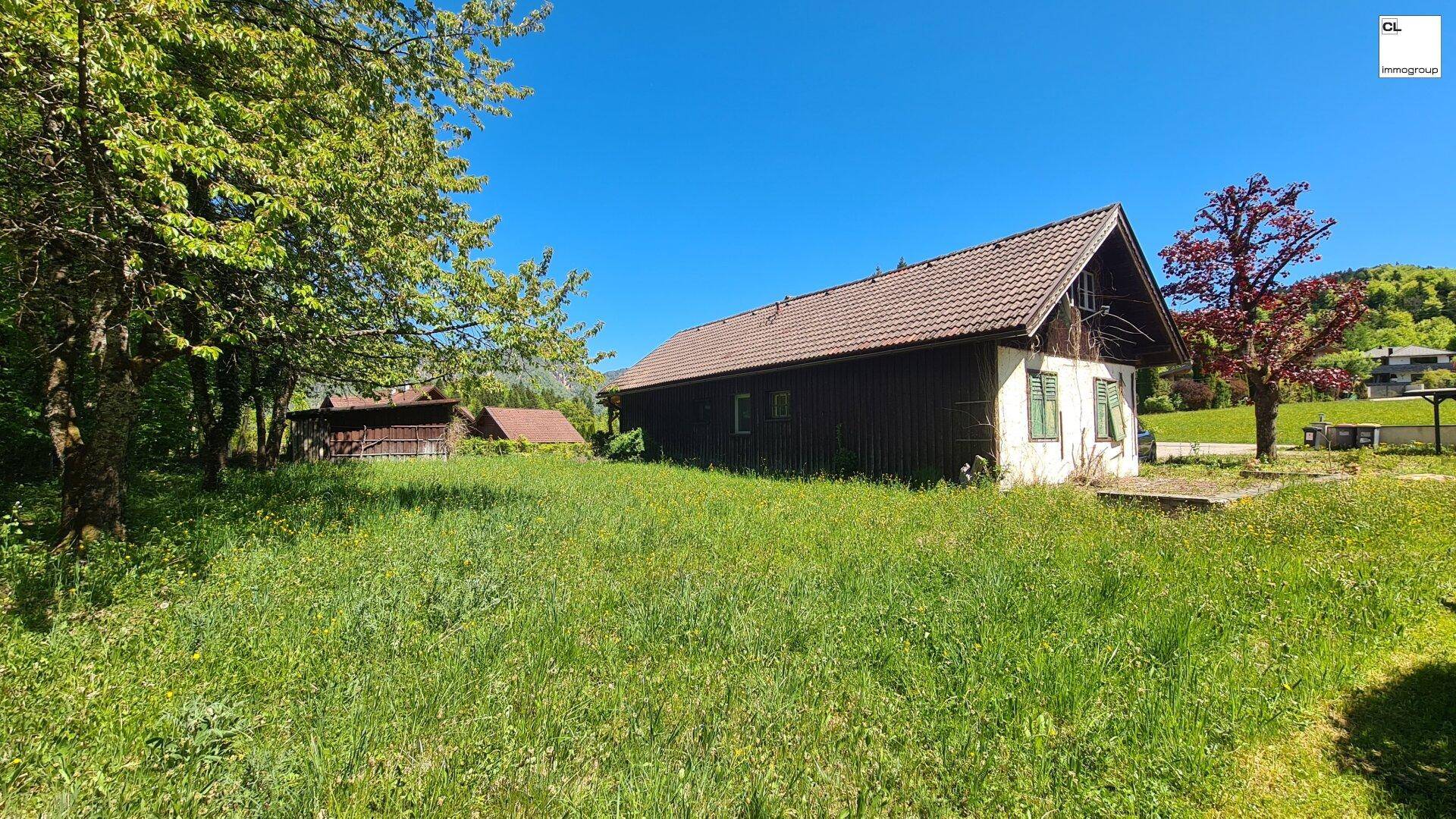 Traditionelles Haus mit brauner Holzfassade und Ziegeldach, umgeben von einer grünen Wiese.