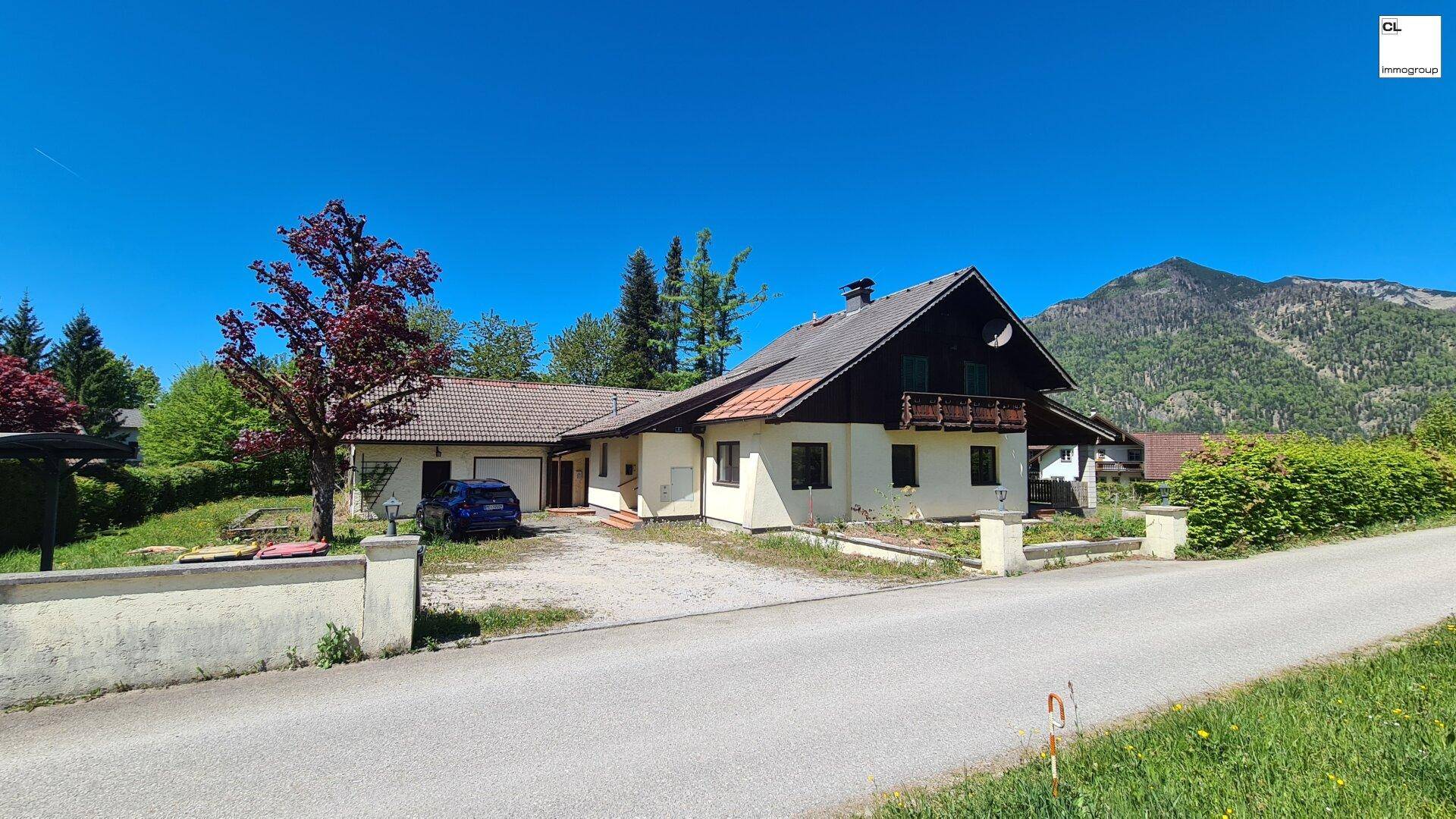 Charmantes Landhaus mit Satteldach, Garage und gepflegtem Vorgarten vor einer Bergkulisse.