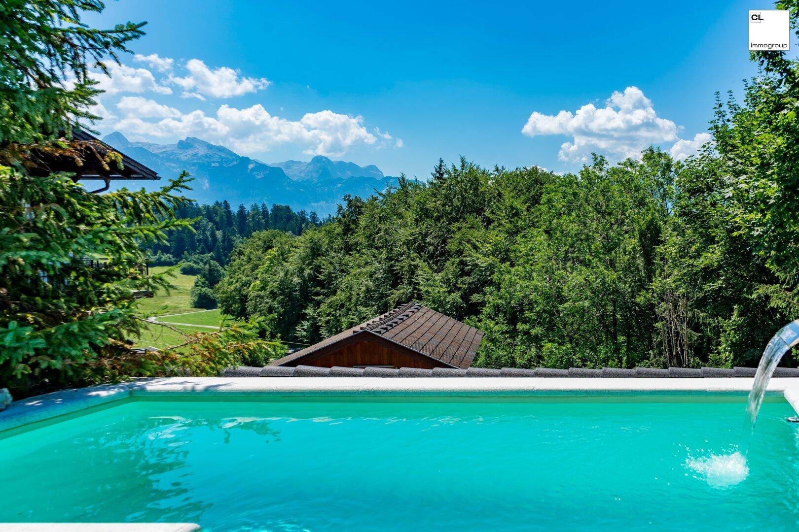 Erfrischender Pool mit weitem Blick über grüne Hügel und ferne Berge unter blauem Himmel.