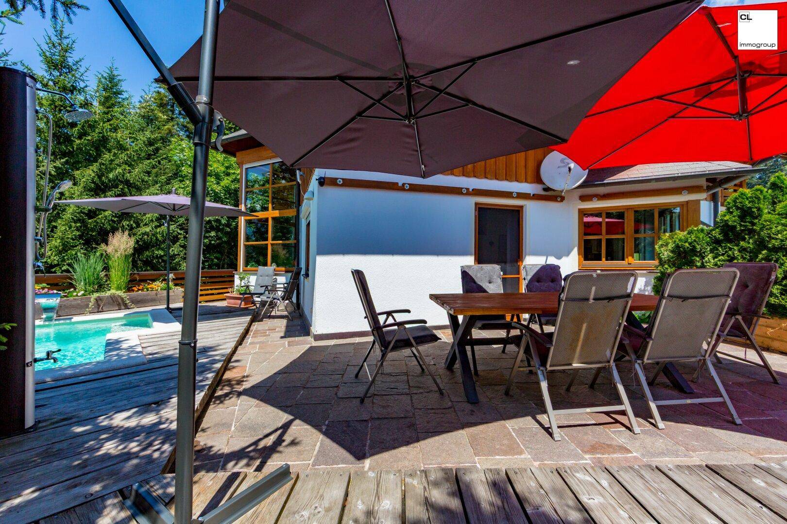 Essbereich auf der Terrasse mit Sonnenschirmen, umgeben von Holzdeck und grüner Hecke.