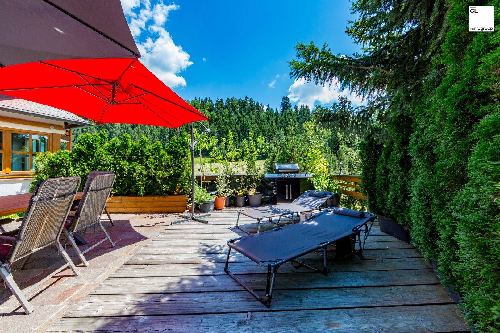 Entspannungsbereich auf der Holzterrasse mit Liegestühlen und Grillplatz, umgeben von Hecken.