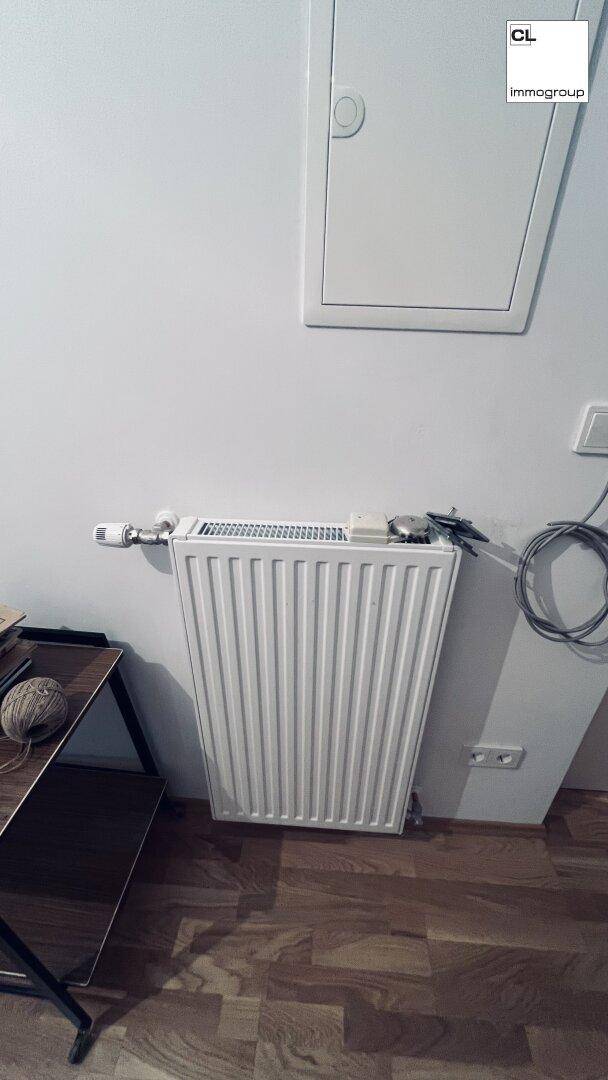 Nahaufnahme eines weißen Heizkörpers unter einer Wandverkleidung in einem Raum mit Holzfußboden.